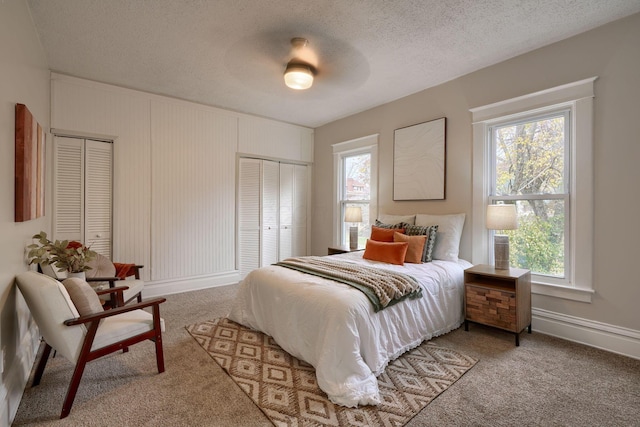 bedroom with two closets, a textured ceiling, carpet floors, and ceiling fan