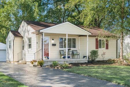 bungalow-style house featuring a garage, covered porch, an outbuilding, and a front lawn