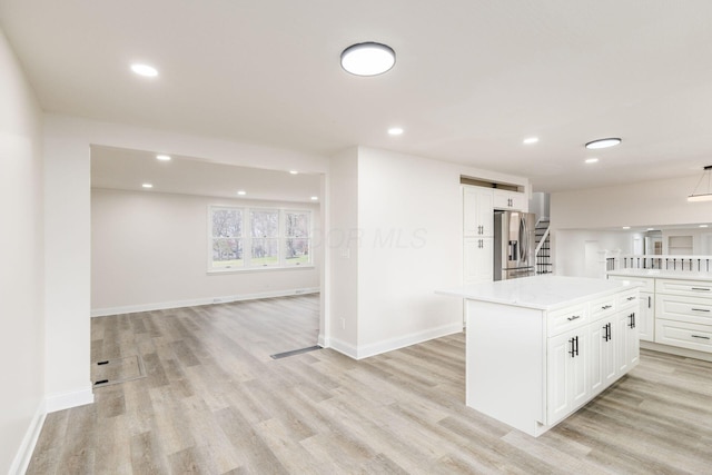 kitchen with light stone countertops, a center island, stainless steel fridge with ice dispenser, white cabinets, and light wood-type flooring