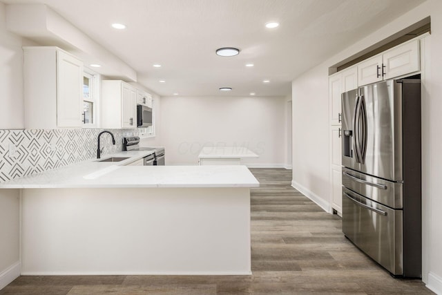 kitchen featuring kitchen peninsula, appliances with stainless steel finishes, sink, light hardwood / wood-style floors, and white cabinetry