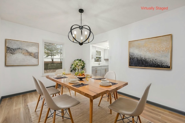 dining area with light wood-type flooring, a notable chandelier, and sink