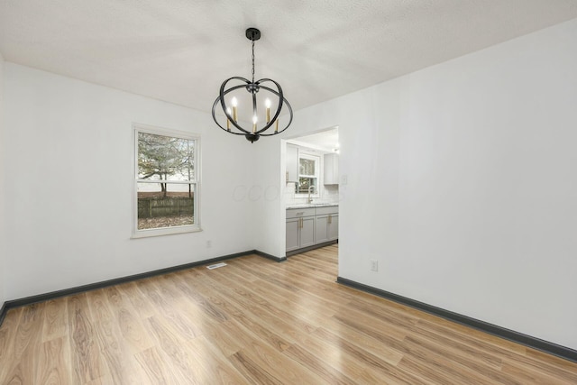 unfurnished dining area with sink, light wood-type flooring, a textured ceiling, and a notable chandelier