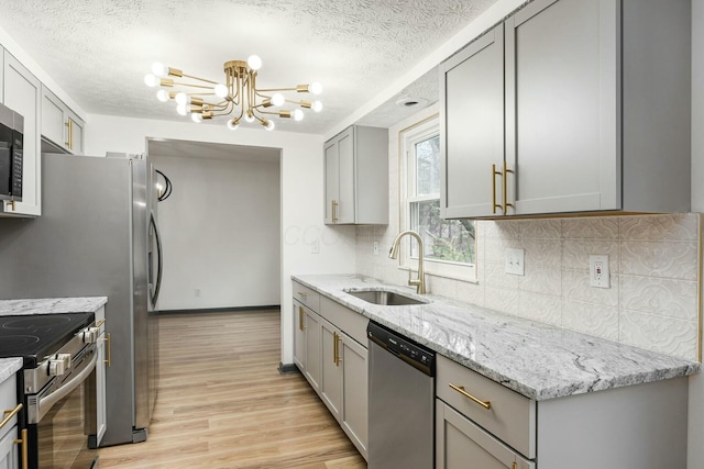 kitchen featuring light stone counters, gray cabinetry, stainless steel appliances, sink, and a notable chandelier