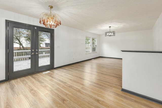 unfurnished dining area featuring french doors, light hardwood / wood-style floors, a textured ceiling, and a notable chandelier