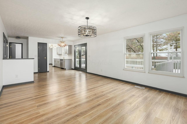 unfurnished living room with a chandelier, light hardwood / wood-style flooring, a healthy amount of sunlight, and sink