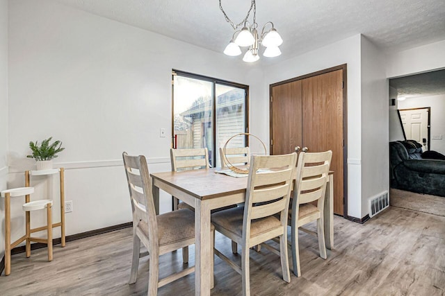 dining room with a chandelier, a textured ceiling, and light wood-type flooring