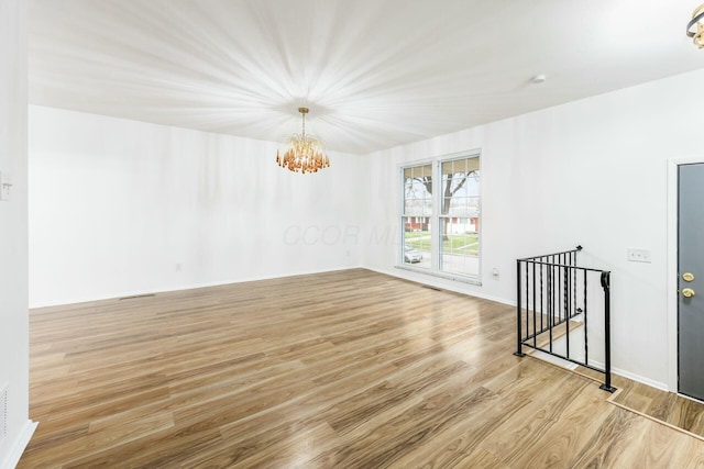 empty room with light hardwood / wood-style floors and a chandelier