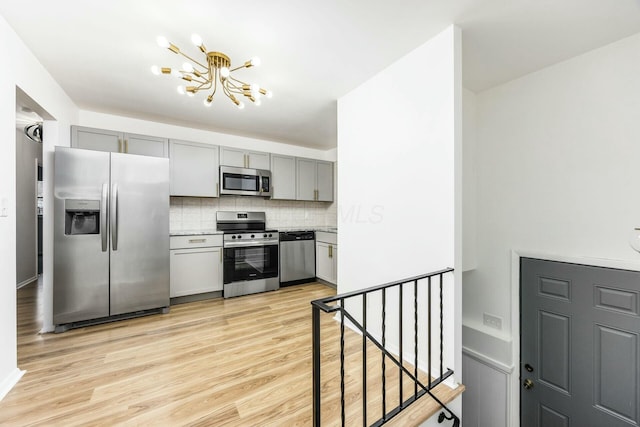 kitchen with backsplash, light hardwood / wood-style flooring, stainless steel appliances, and a notable chandelier