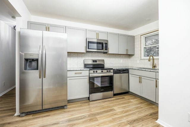 kitchen featuring sink, stainless steel appliances, light stone counters, light hardwood / wood-style flooring, and backsplash