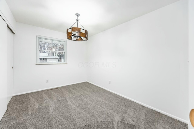 carpeted spare room with an inviting chandelier