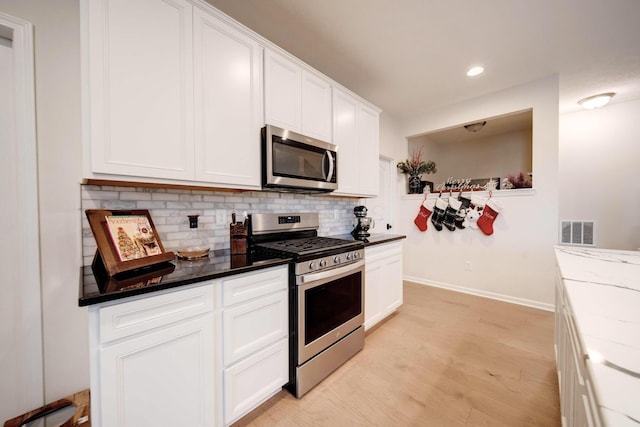 kitchen with decorative backsplash, appliances with stainless steel finishes, light stone countertops, white cabinets, and light hardwood / wood-style floors