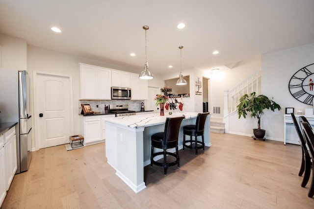 kitchen with a center island, hanging light fixtures, light wood-type flooring, and appliances with stainless steel finishes