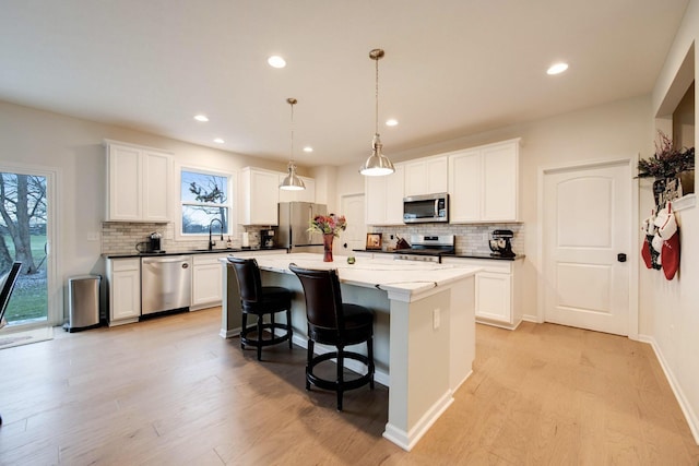 kitchen featuring a kitchen island, stainless steel appliances, decorative light fixtures, and light hardwood / wood-style floors