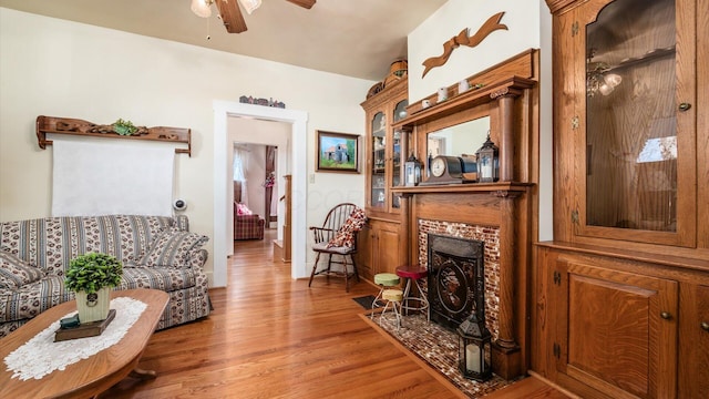 living room featuring ceiling fan, wood-type flooring, and a brick fireplace