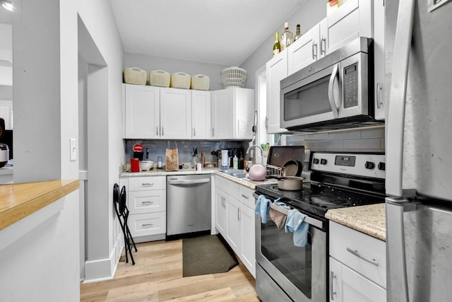 kitchen with white cabinets, stainless steel appliances, light hardwood / wood-style flooring, and sink