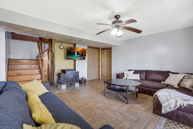 living room featuring ceiling fan, a wood stove, and light parquet flooring