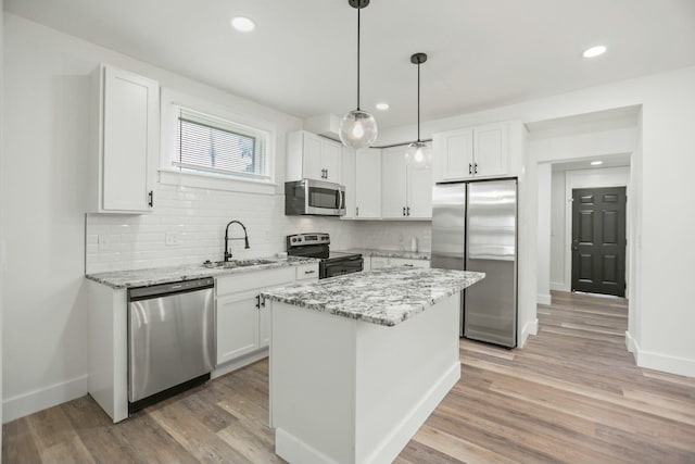 kitchen featuring appliances with stainless steel finishes, light stone counters, a kitchen island, hardwood / wood-style floors, and white cabinetry