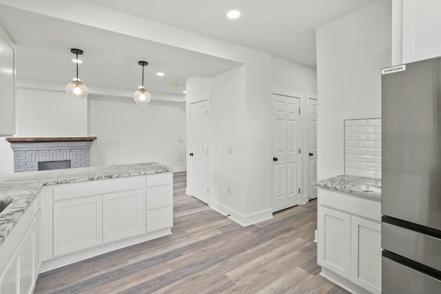 kitchen featuring stainless steel refrigerator, hanging light fixtures, light stone counters, light hardwood / wood-style floors, and white cabinets