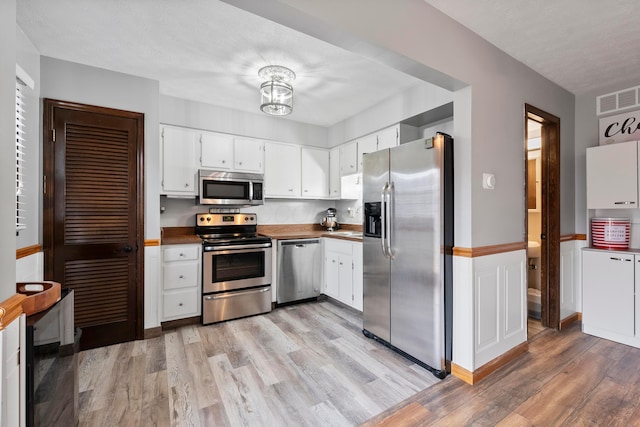 kitchen with a textured ceiling, stainless steel appliances, white cabinetry, and light hardwood / wood-style flooring