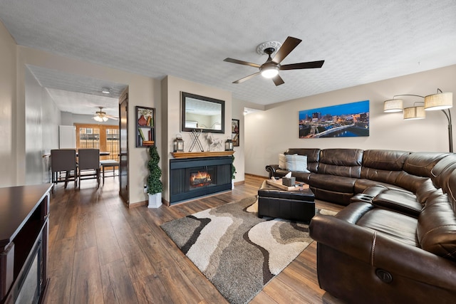 living room with a textured ceiling, ceiling fan, and dark wood-type flooring