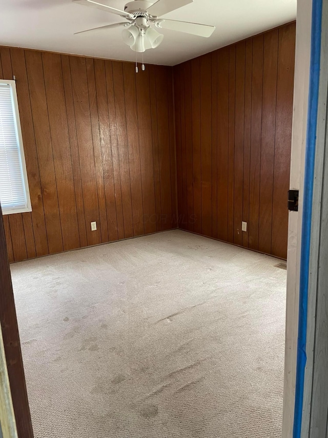 carpeted spare room featuring ceiling fan and wood walls