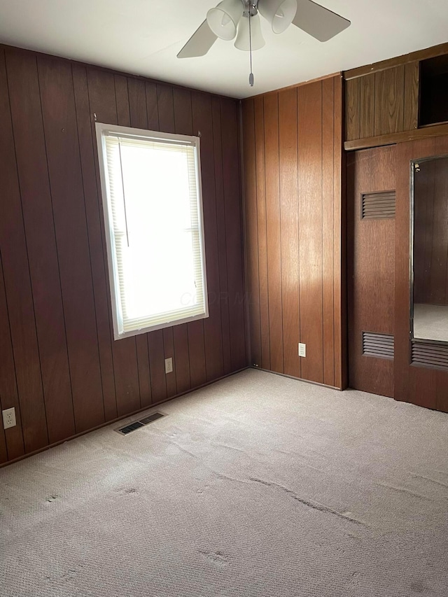 unfurnished bedroom featuring ceiling fan, wood walls, and light carpet