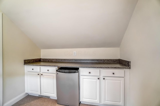 kitchen featuring carpet, white cabinetry, and vaulted ceiling