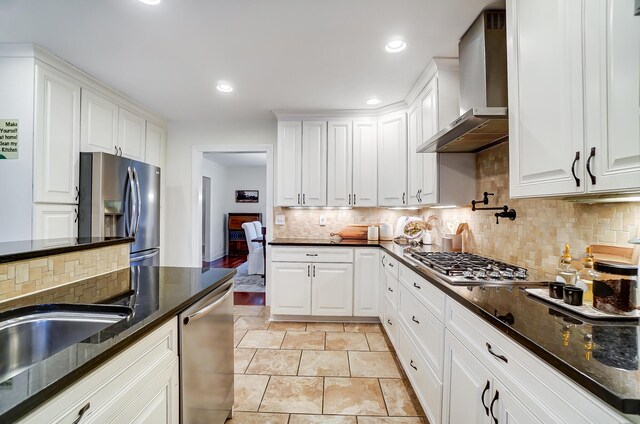 kitchen with white cabinets, dark stone countertops, wall chimney range hood, and appliances with stainless steel finishes