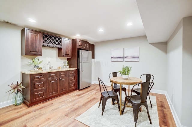 kitchen featuring light stone countertops, stainless steel fridge, dark brown cabinetry, sink, and light hardwood / wood-style flooring