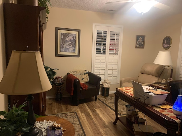 living area featuring ceiling fan, light hardwood / wood-style flooring, and a textured ceiling