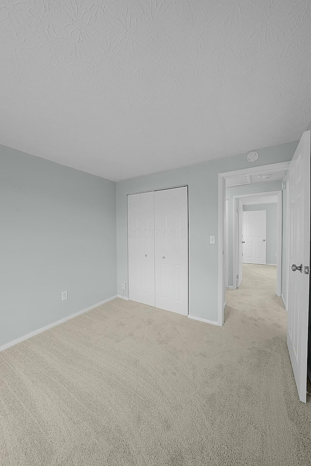 unfurnished bedroom featuring a textured ceiling, light colored carpet, and a closet