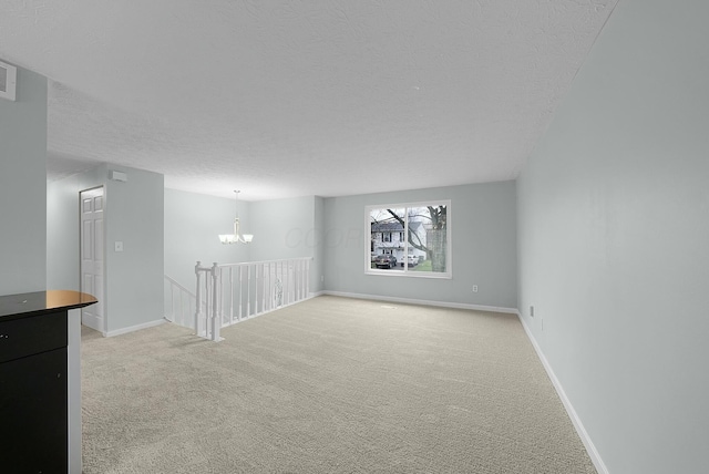 carpeted empty room with a textured ceiling and an inviting chandelier