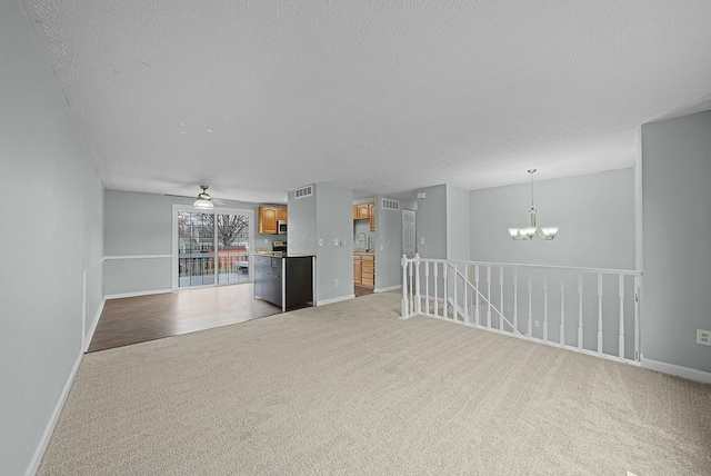 unfurnished living room featuring light carpet, sink, ceiling fan with notable chandelier, and a textured ceiling