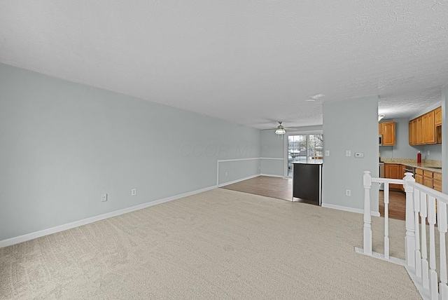 unfurnished living room featuring ceiling fan, light colored carpet, and a textured ceiling