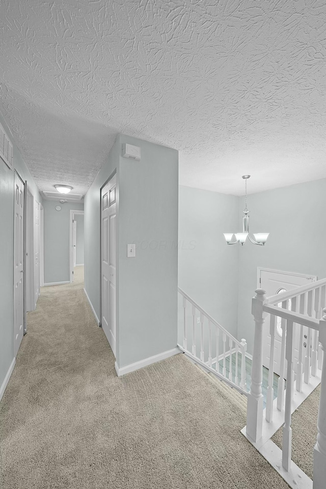 corridor featuring carpet, a textured ceiling, and a chandelier