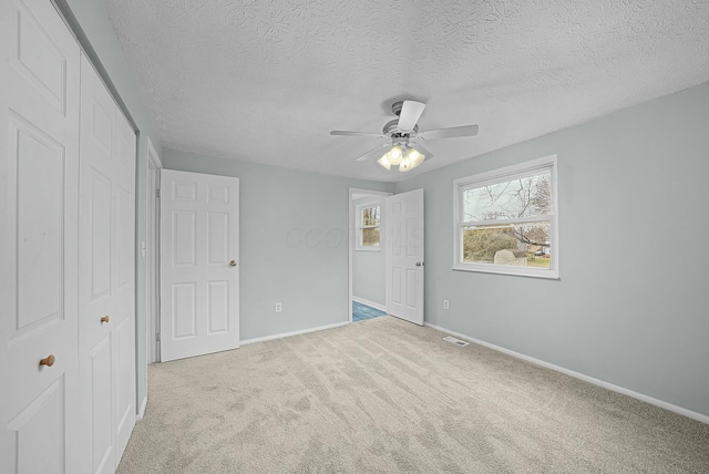 unfurnished bedroom featuring ceiling fan, a closet, light carpet, and a textured ceiling