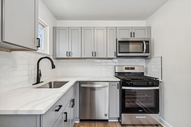 kitchen with gray cabinetry, light hardwood / wood-style floors, light stone countertops, and appliances with stainless steel finishes