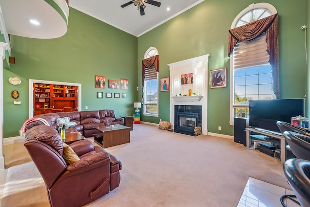 living room with crown molding, carpet flooring, ceiling fan, a towering ceiling, and a fireplace