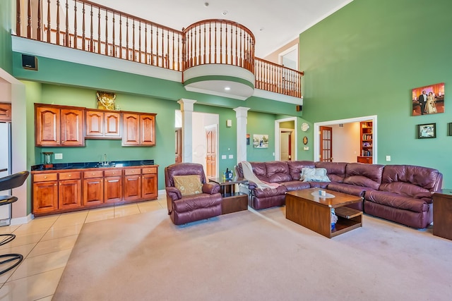 tiled living room featuring ornate columns, sink, and a high ceiling