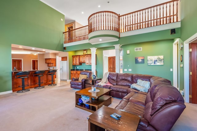 living room with decorative columns, a towering ceiling, and light colored carpet