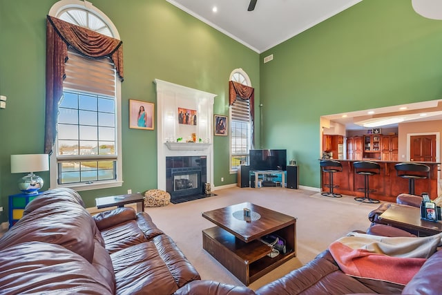 carpeted living room featuring a tile fireplace, crown molding, high vaulted ceiling, and ceiling fan