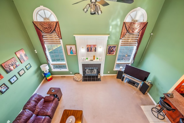 living room featuring carpet, a tiled fireplace, ceiling fan, and a towering ceiling