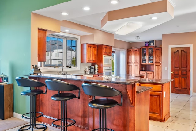 kitchen featuring kitchen peninsula, a breakfast bar, white appliances, light tile patterned floors, and a kitchen island