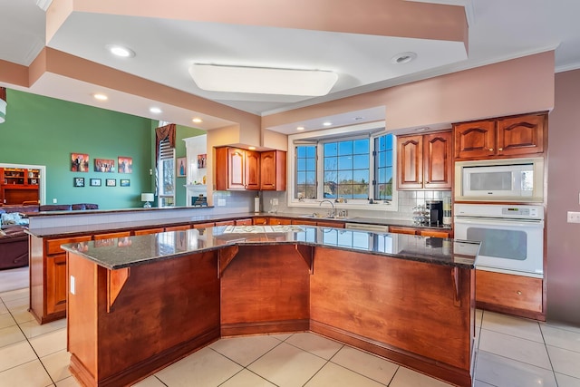 kitchen with white appliances, sink, light tile patterned floors, a kitchen island, and kitchen peninsula