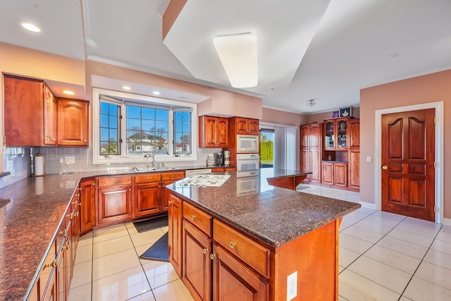 kitchen featuring sink, light tile patterned flooring, backsplash, white appliances, and a kitchen island