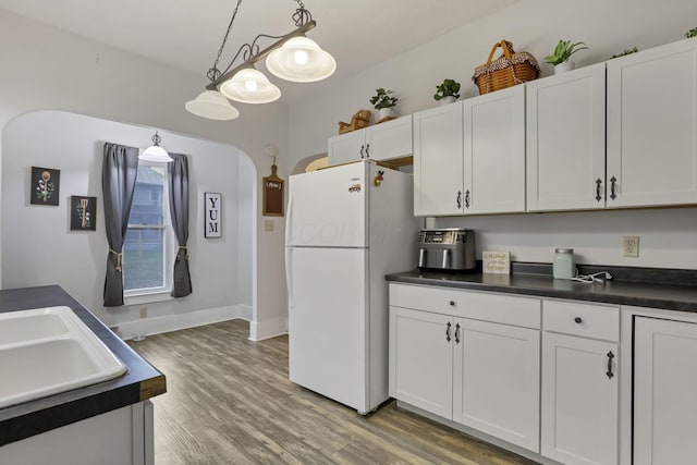 kitchen featuring white cabinets, white fridge, hanging light fixtures, and hardwood / wood-style flooring