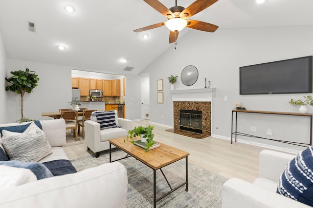 living room with high vaulted ceiling, ceiling fan, a high end fireplace, and light hardwood / wood-style flooring