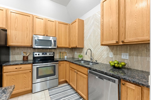 kitchen with appliances with stainless steel finishes, light tile patterned floors, dark stone countertops, and sink