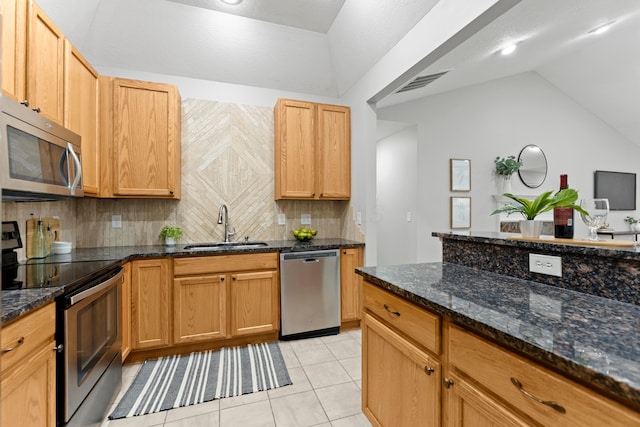 kitchen featuring lofted ceiling, dark stone counters, sink, appliances with stainless steel finishes, and tasteful backsplash