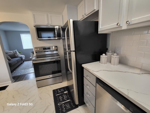 kitchen with white cabinetry, stainless steel appliances, light stone counters, backsplash, and light wood-type flooring